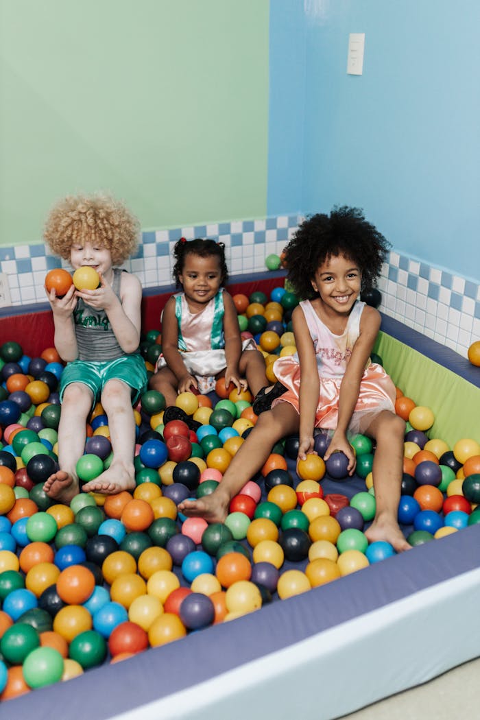 Joyful children with curly hair playing in a vibrant indoor ball pit.